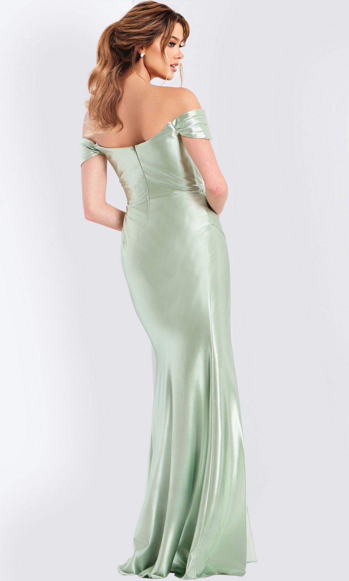 A woman poses with her back to the camera in a light green, off-the-shoulder Jovani 47863 long prom dress featuring a high-leg side slit, set against a plain light background.